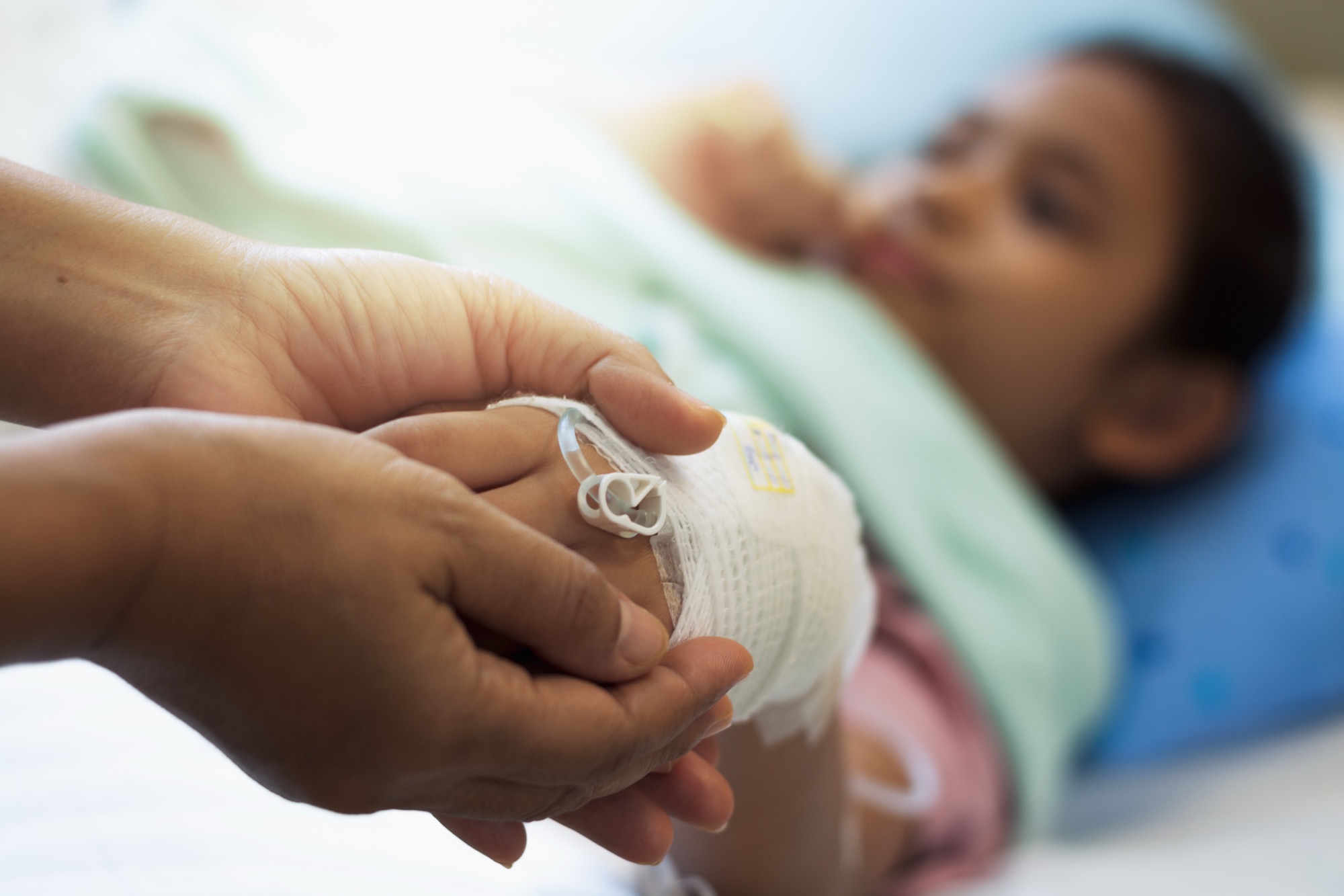 A mother holds the bandaged hand of her child resting in a hospital bed.